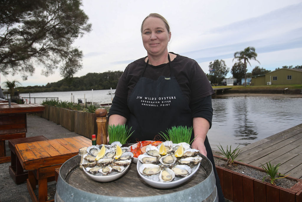 Woman in apron holding plates of fresh oysters at Jim Wild's Oysters in Jervis Bay.