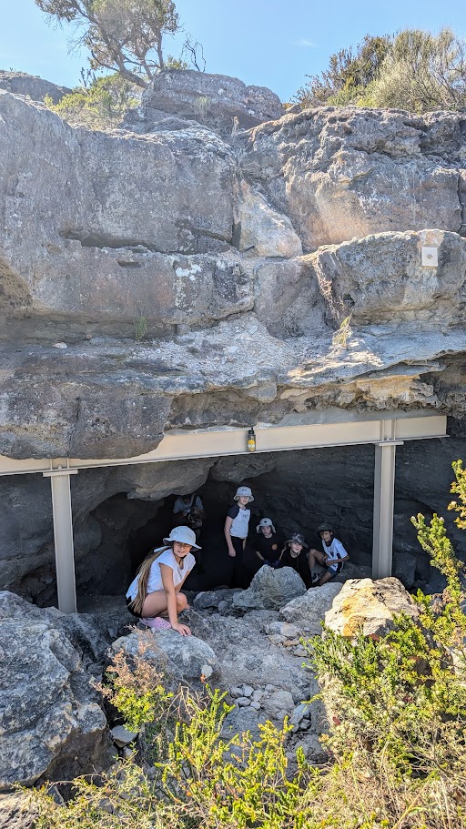 A group of people gathers at the entrance of a cave or tunnel along the Jervis Bay coastline.