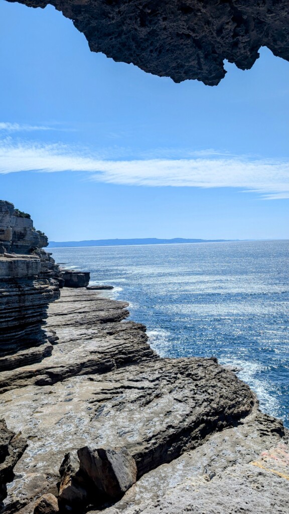 Rugged coastal cliffs meet the ocean under a blue sky in Jervis Bay.