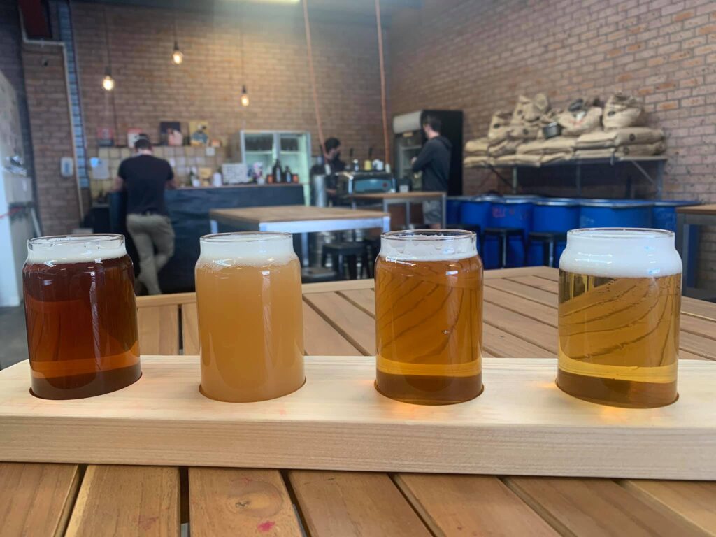 Four glasses of different coloured beers on a wooden paddle in a brewery.