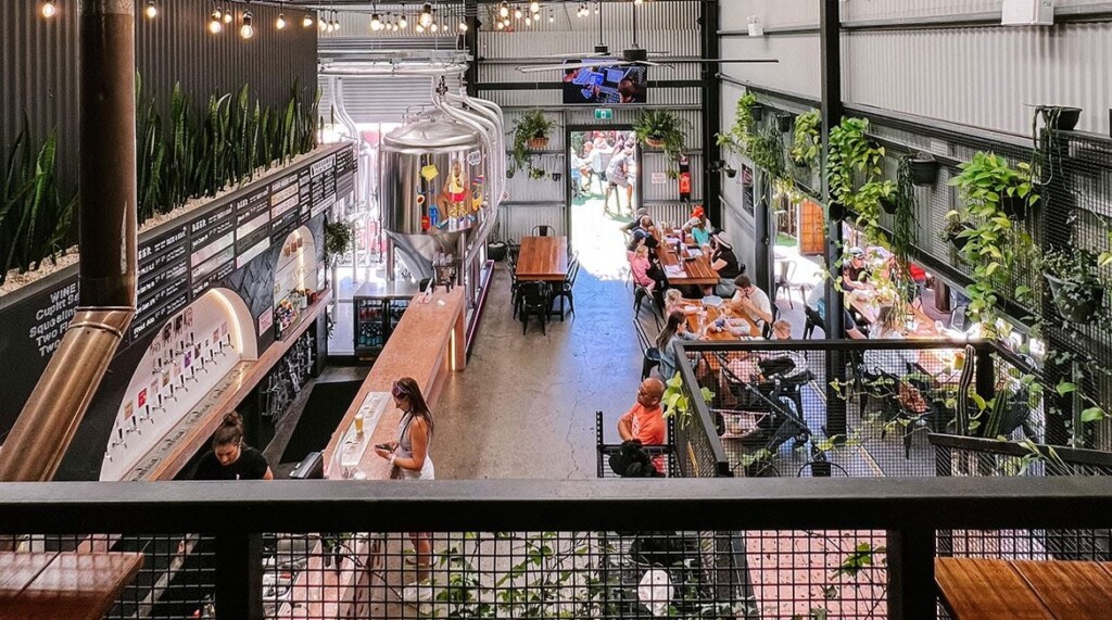 Interior view of a modern brewery with brewing equipment, bar, and seating areas.