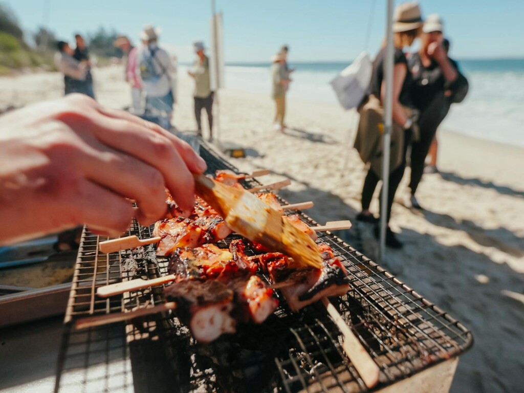 A chef grilling fresh octopus skewers on a beachside barbecue during the Coastal Forage event in Jervis Bay.