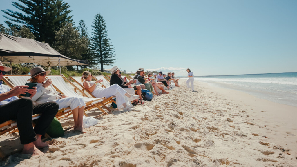 Guests relaxing in white deck chairs on the white sand beach of Jervis Bay during the Coastal Forage culinary tour.