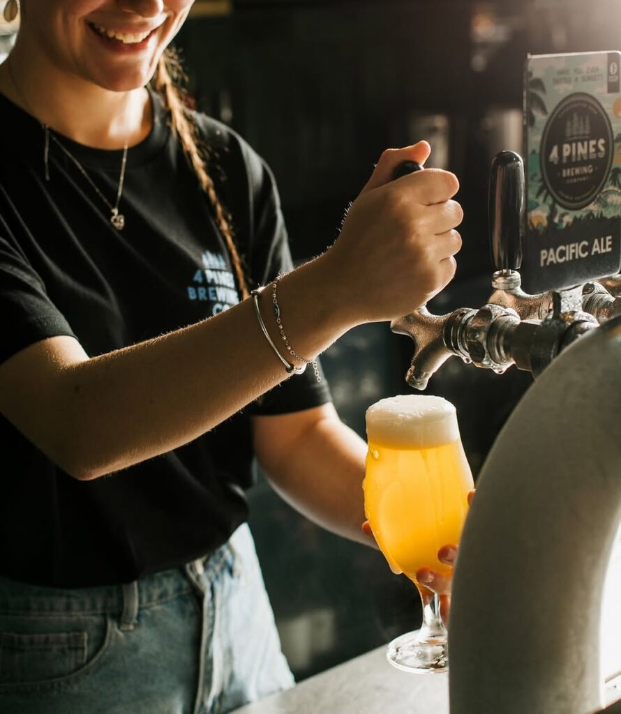 A smiling bartender pouring a fresh, frosty pint of 4 Pines craft beer on tap at the Kangaroo Valley Craft Beer and BBQ Festival.