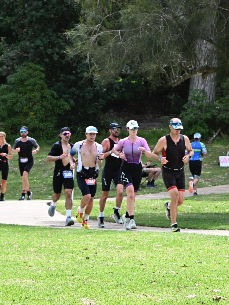 A group of focused athletes run together along a coastal park pathway during the final running leg of the Shimano Husky Triathlon Festival in Huskisson.