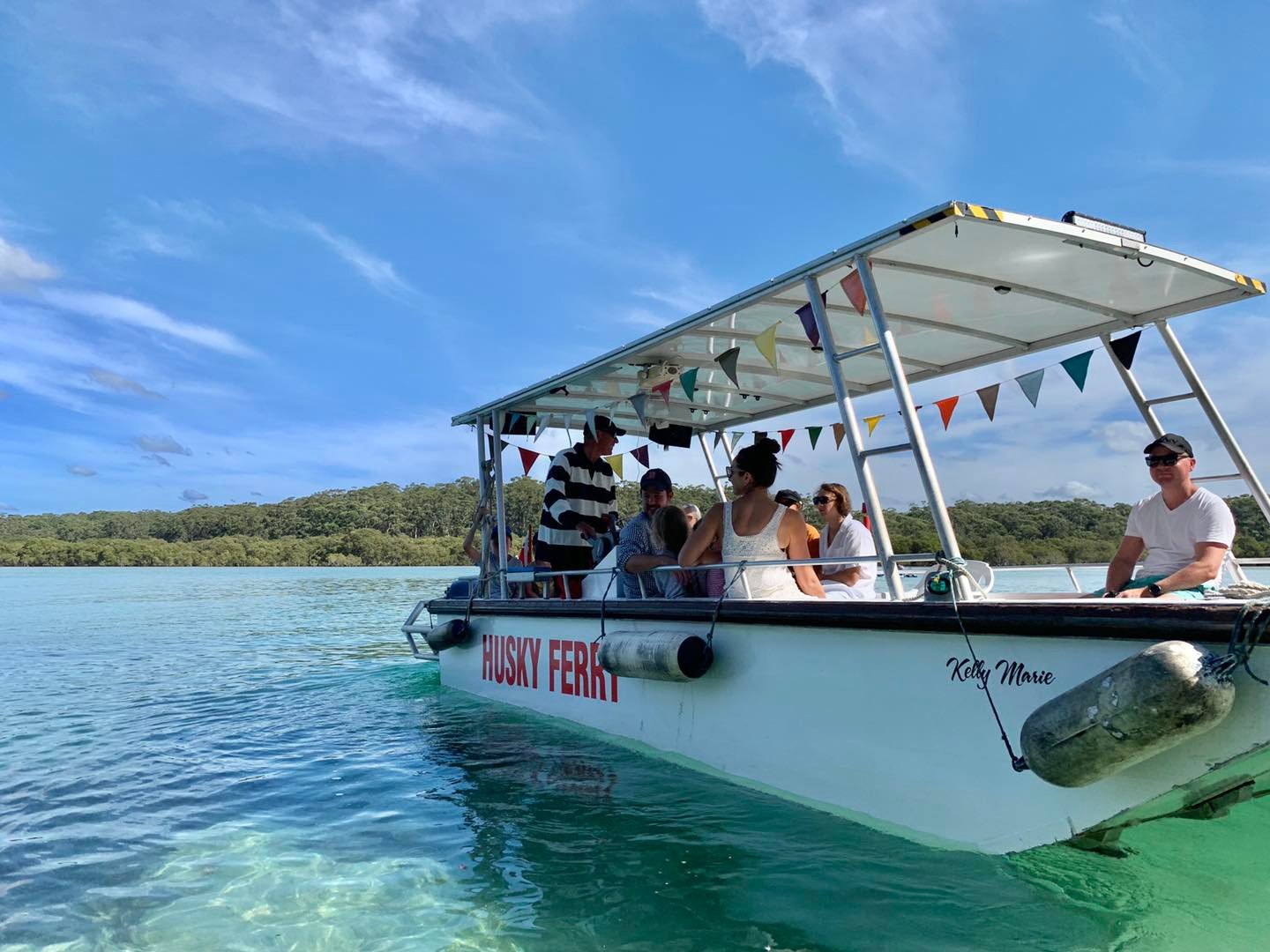 The Husky Ferry boat Kelly Marie cruising through the bright turquoise waters of Currambene Creek in Jervis Bay under a blue sky.