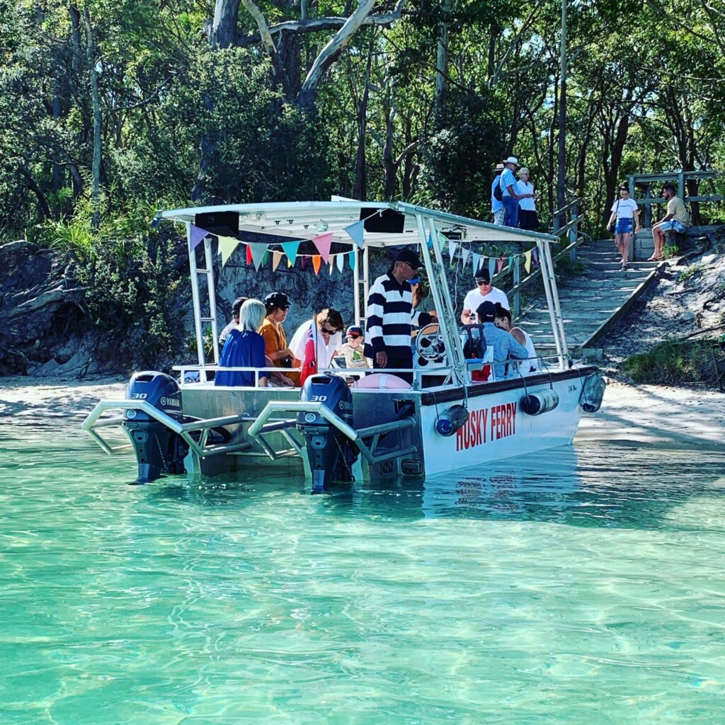 The Husky Ferry Kelly Marie boat landing on a sandy beach in clear turquoise water at Jervis Bay