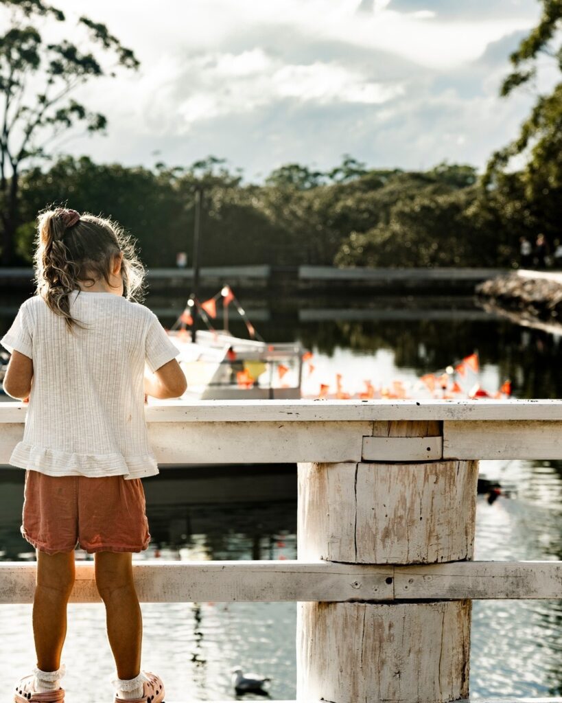 A young girl looking over a rustic white wooden railing at boats on the pond outside the Jervis Bay Maritime Museum in Huskisson.