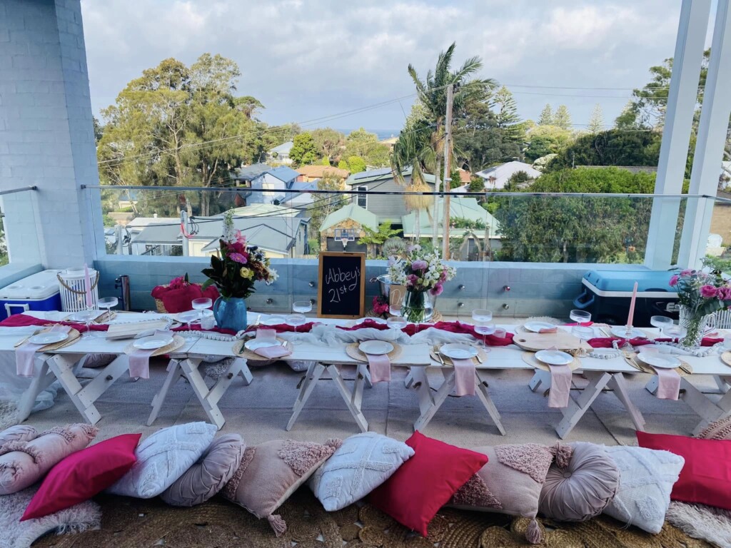 Long luxury picnic table setup for a 21st birthday party on a glass balcony with ocean views in Jervis Bay.