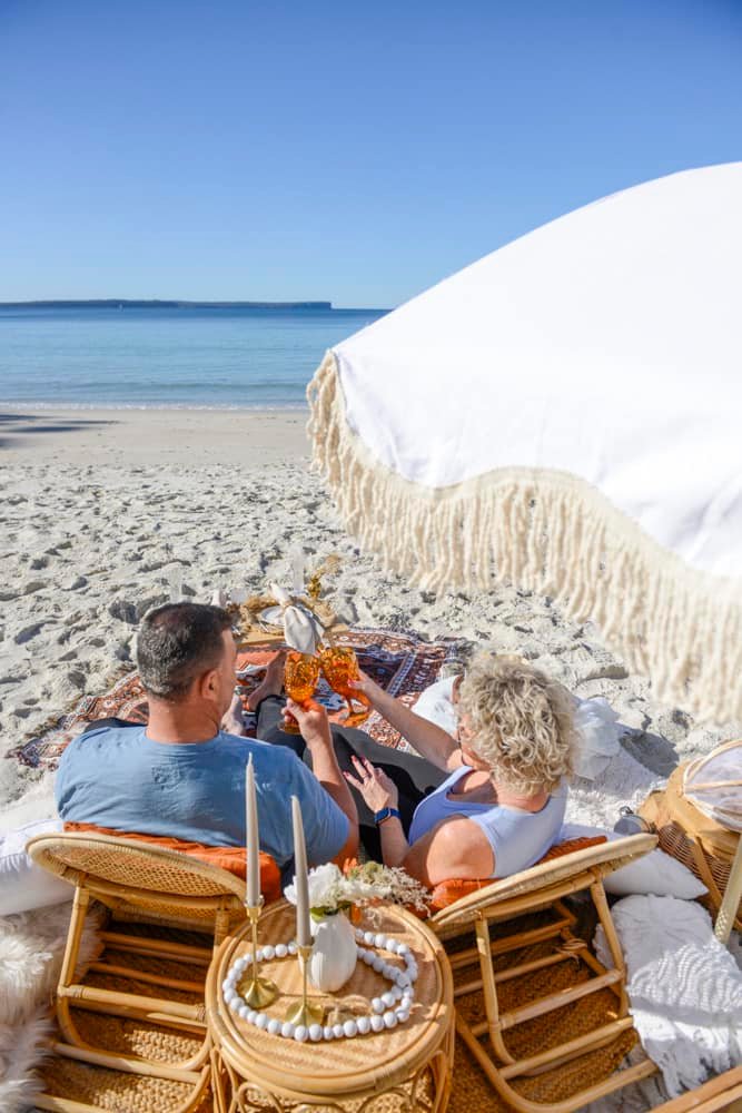 Couple toasting glasses at a romantic luxury beach picnic on the famous white silica sands of Jervis Bay.