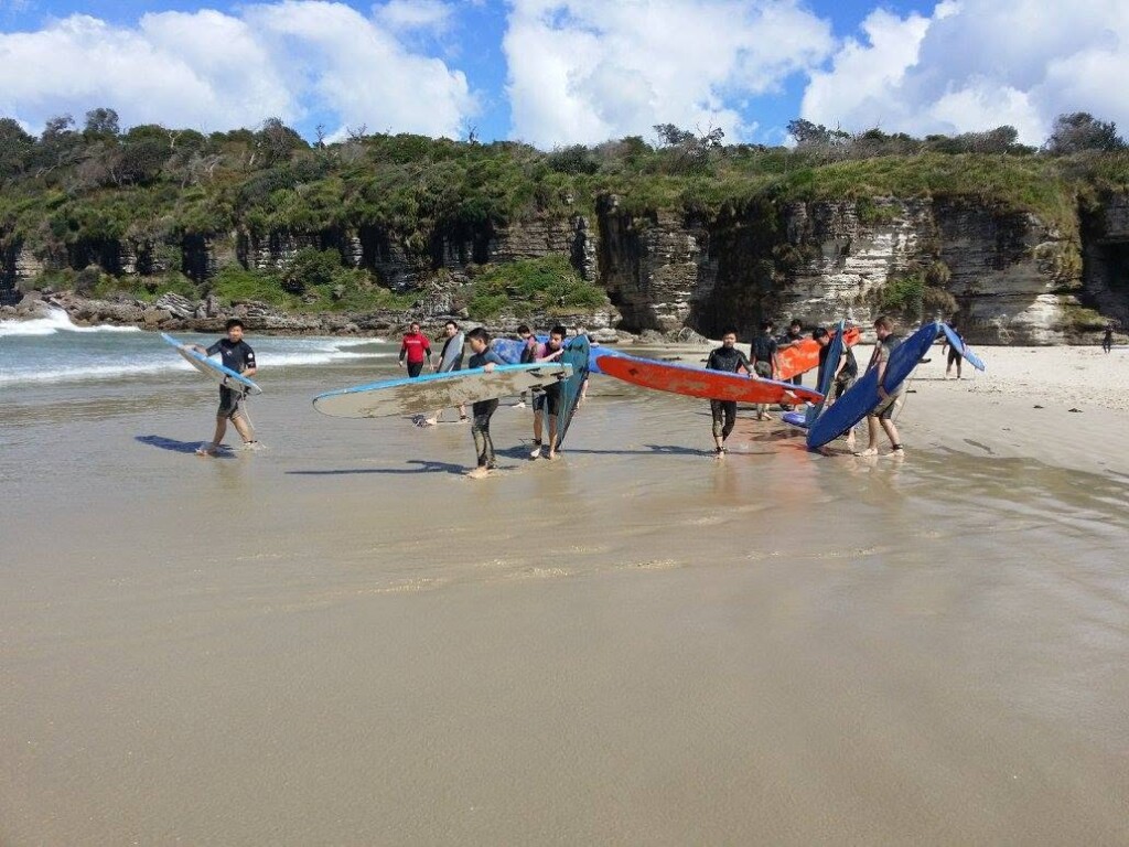 A group of surf students carrying their colorful longboards across the wet sand toward the ocean at Jervis Bay.