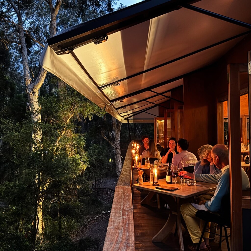Diners sitting at candlelit wooden tables on the elevated deck of The Gunyah at dusk.