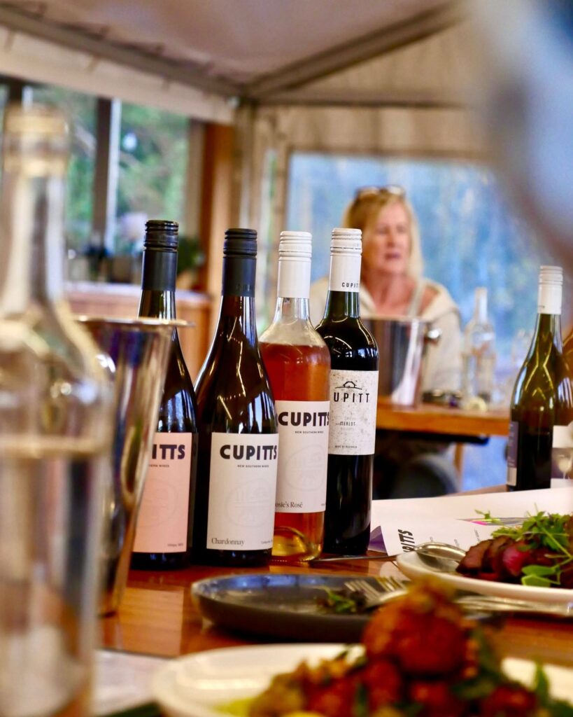 A row of Cupitt's Estate wine bottles on a dining table with a softly blurred background of a diner and windows.