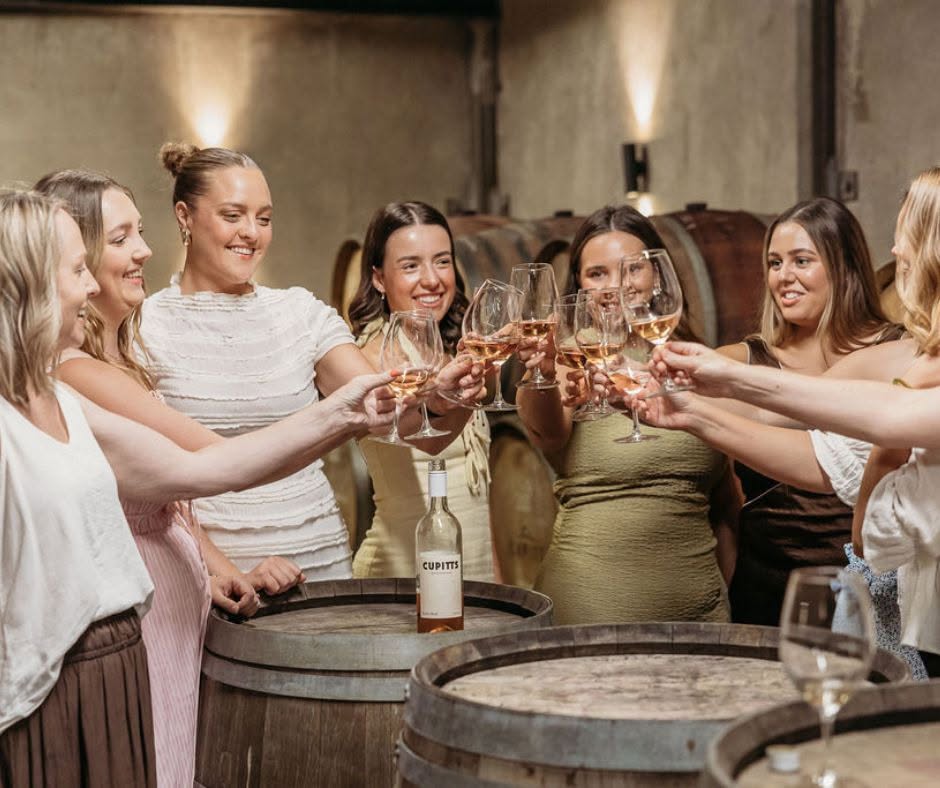 A group of women toasting with wine glasses over wooden barrels inside the Cupitt's Estate cellar.