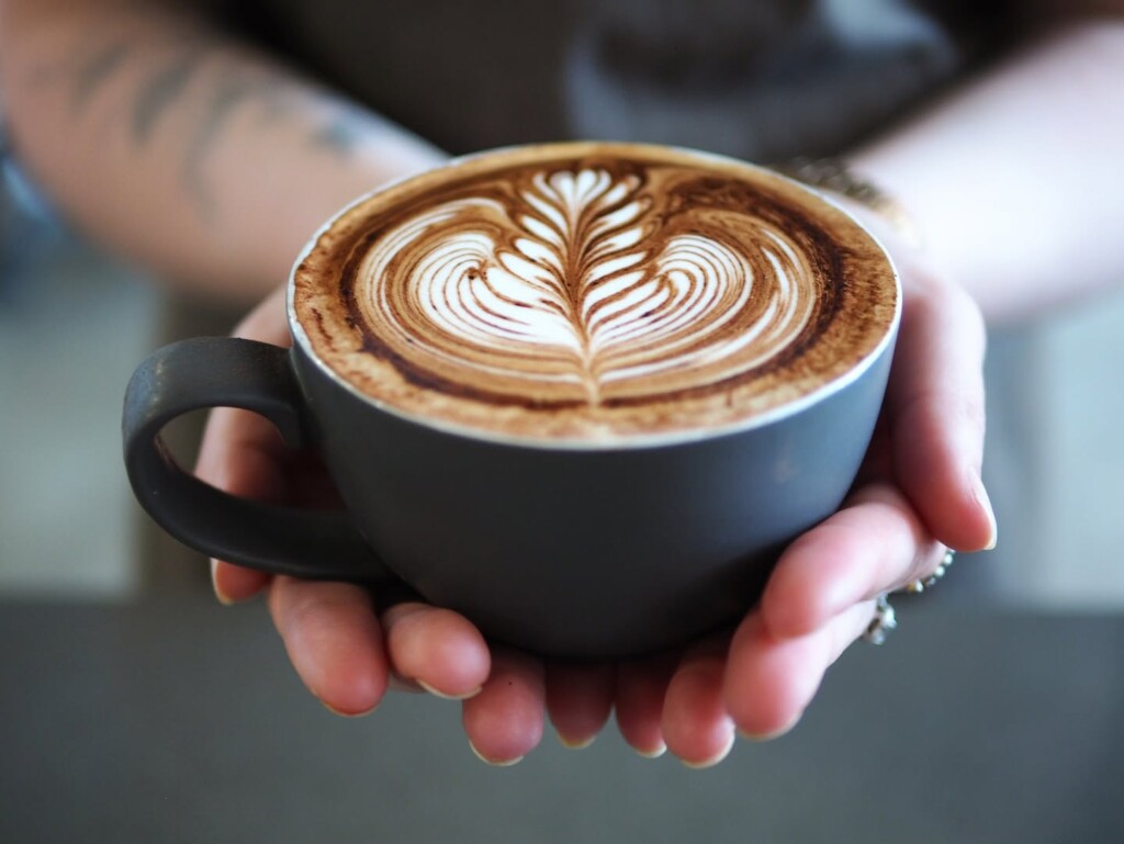 Barista holding a freshly made latte with latte art at 5 Little Pigs café in Huskisson, NSW.