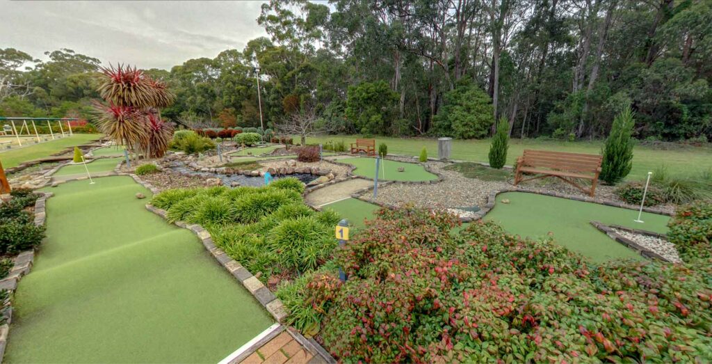 The 18-hole mini golf course at Husky Sports on an overcast day, showing undulating synthetic greens lined with bricks, native shrubs, and tall eucalyptus trees in the background.