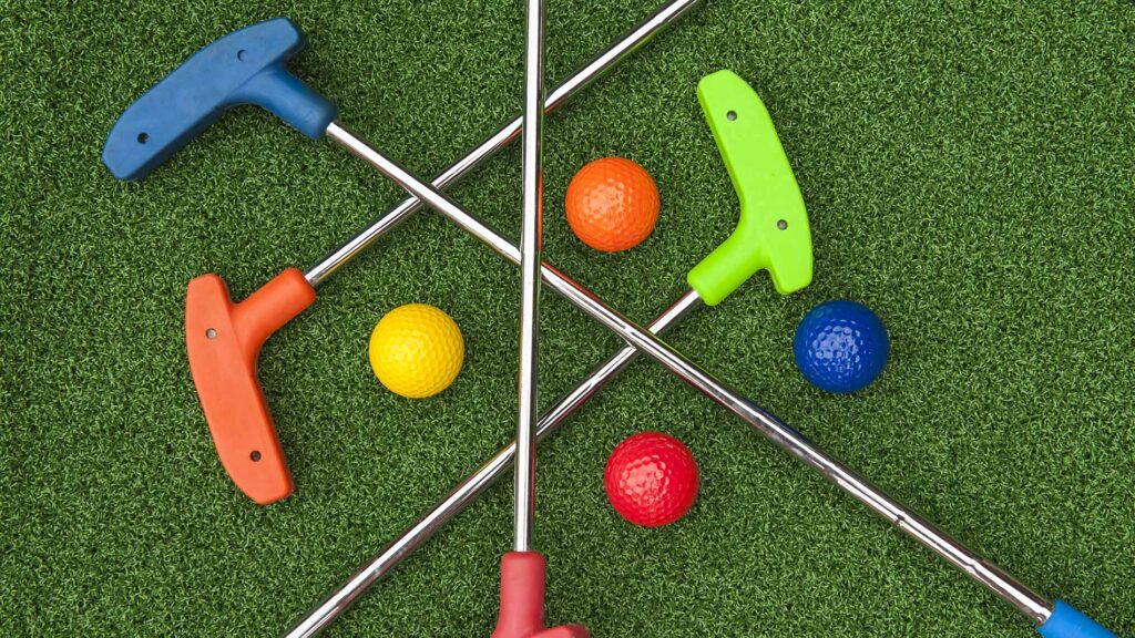 Four brightly colored rubber-headed mini golf putters and matching dimpled balls resting on synthetic green turf.