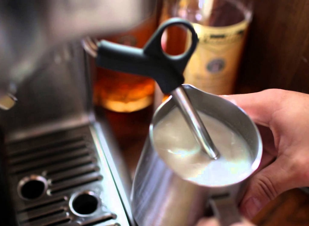 Barista steaming milk beside an espresso machine at Angels Bayside