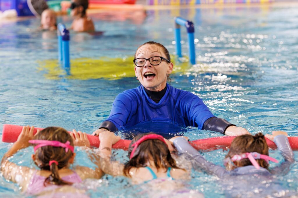 Children taking part in a swimming lesson with an instructor in an indoor pool