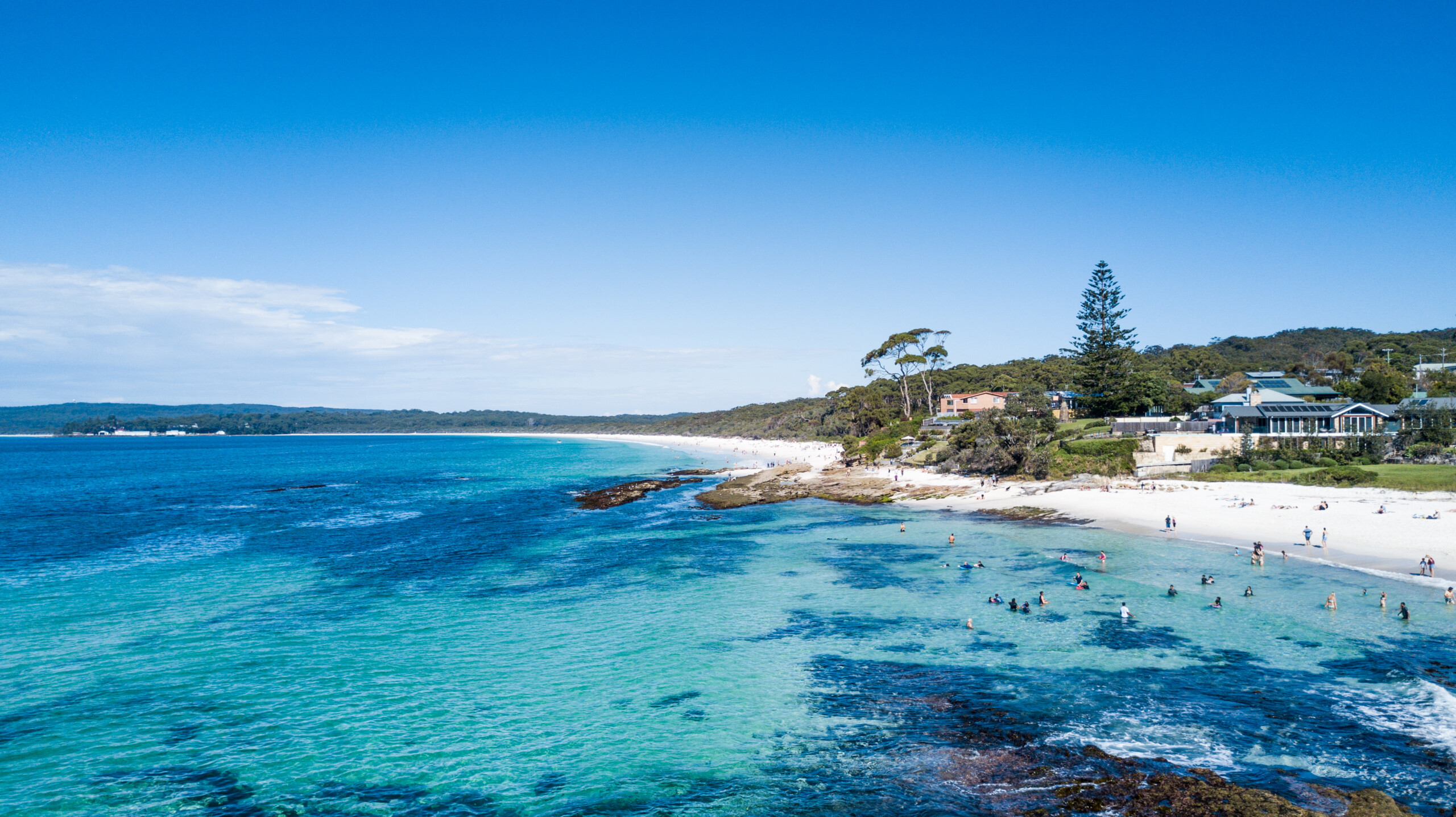 Aerial view of Hyams Beach with white sand, clear turquoise water and coastal homes in Jervis Bay