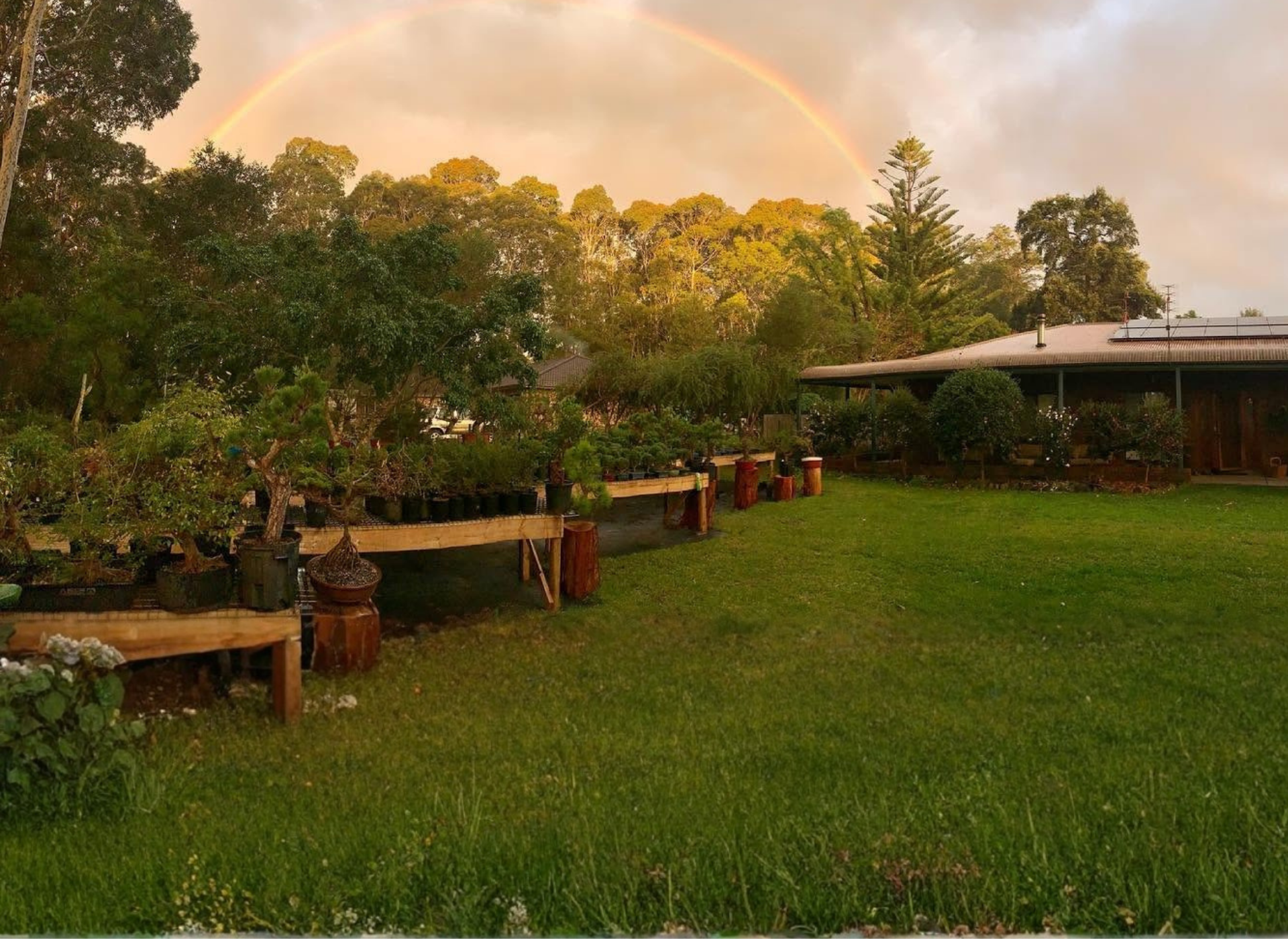 Rainbow over a lush garden and landscaped grounds surrounded by trees