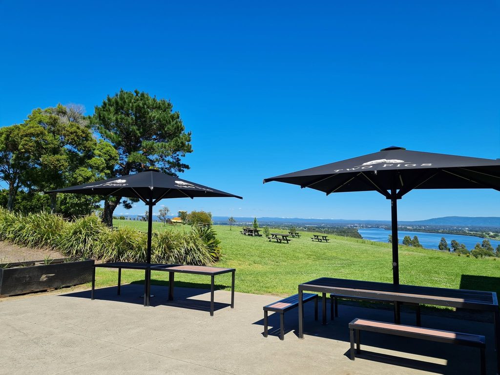 Outdoor seating at Two Figs Winery overlooking green countryside, water, and distant mountains.