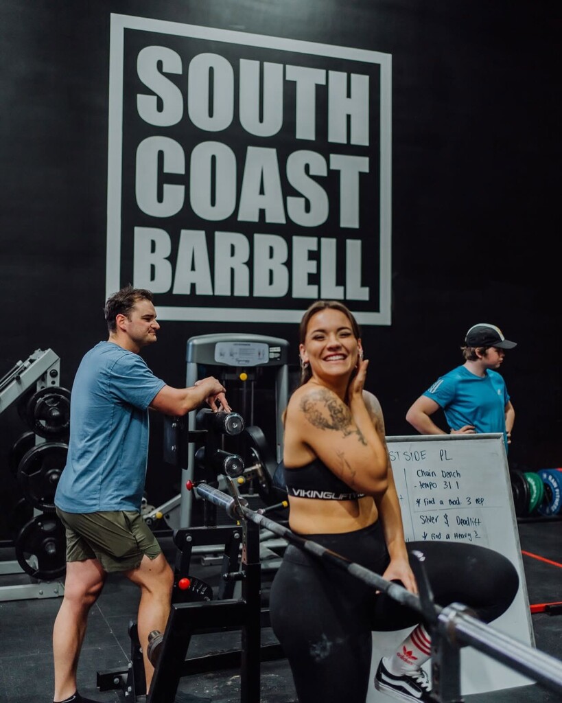 Woman preparing to perform a barbell deadlift inside South Coast Barbell's strength training gym.