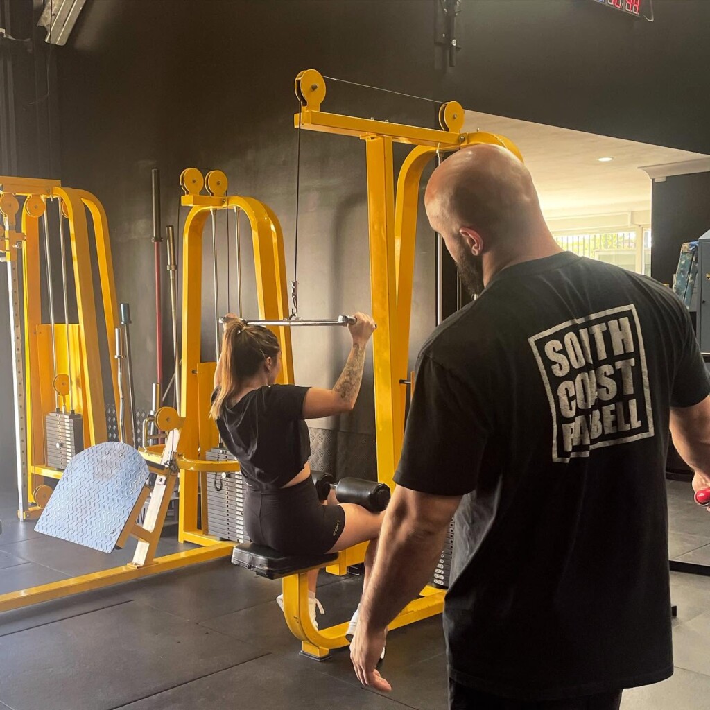 Weightlifting benches, squat racks, barbells, and weight plates inside South Coast Barbell gym in Huskisson.