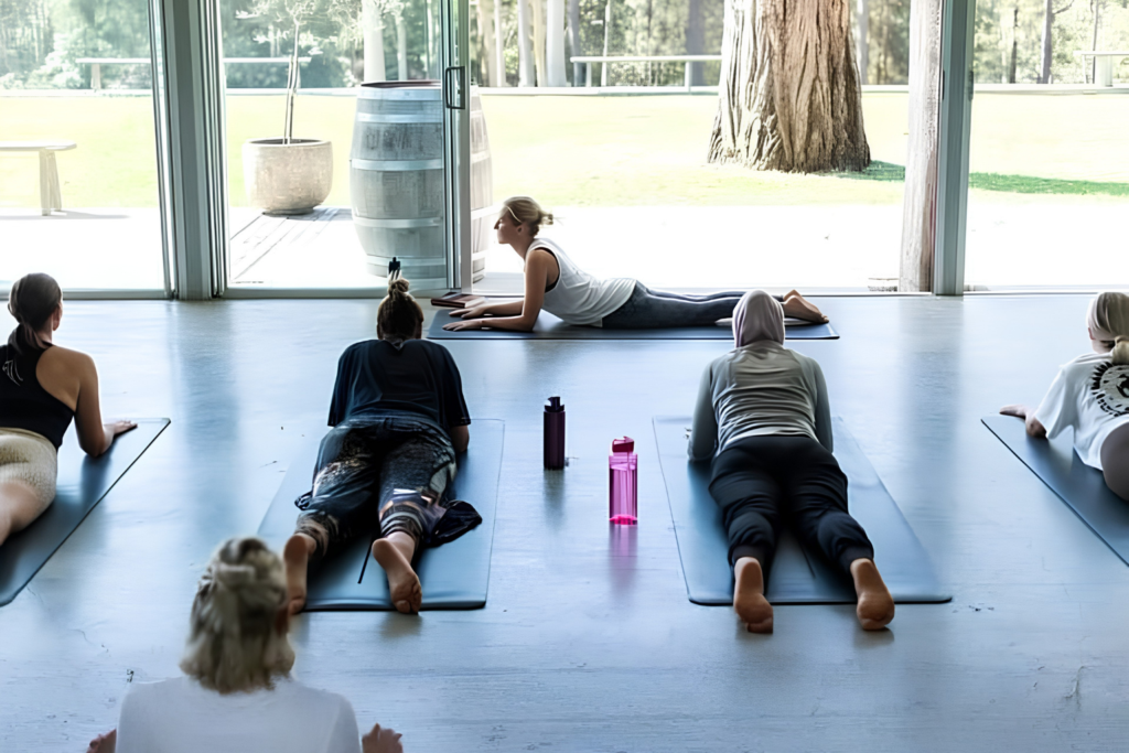 Participants practising core strength and balance exercises on mats during a fitness class in a Pilates studio.