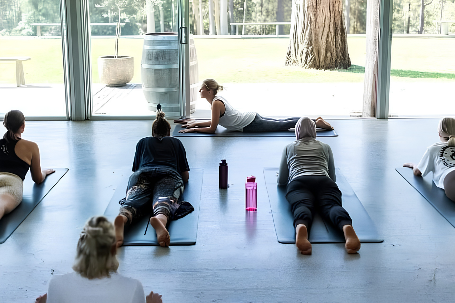 Participants practising core strength and balance exercises on mats during a fitness class in a Pilates studio.