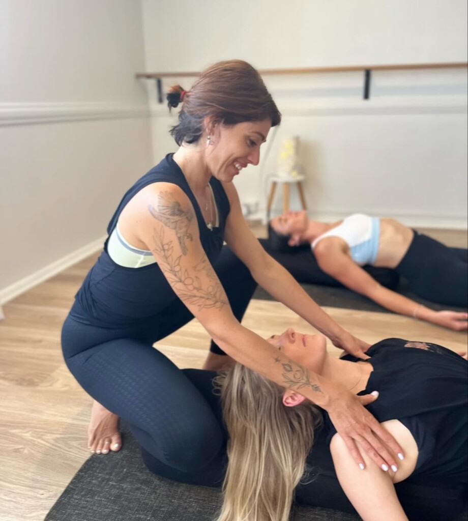 Women participating in a group Pilates session, sitting on exercise mats in a bright studio.
