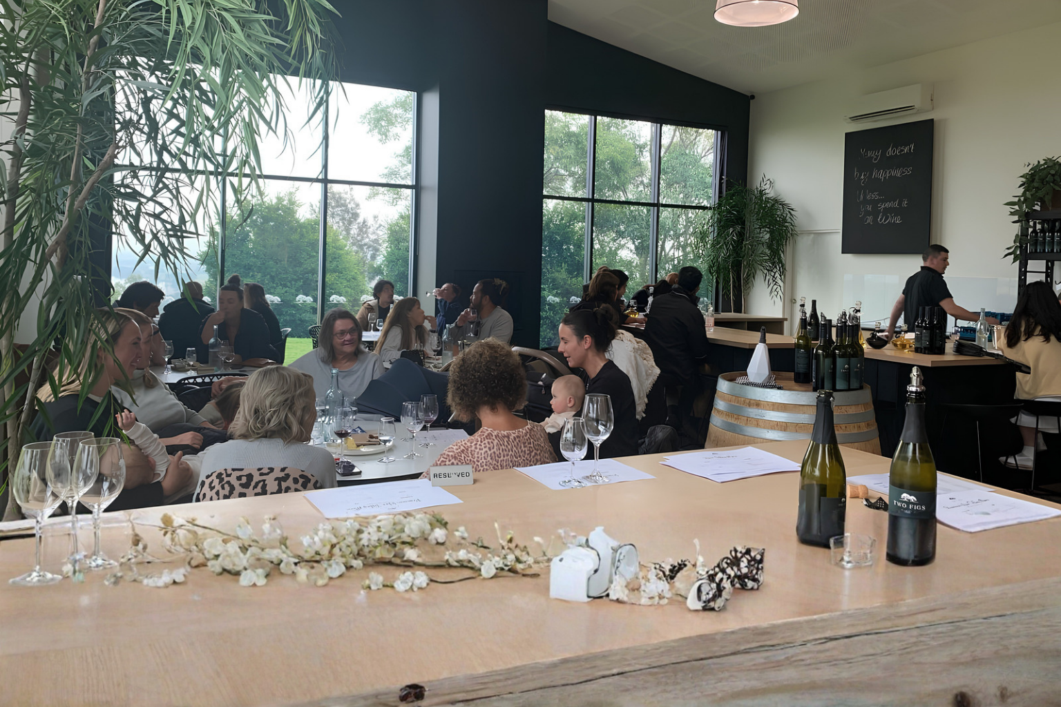 Guests enjoying a wine tasting at Two Figs Winery in a bright cellar door with large windows overlooking the countryside.